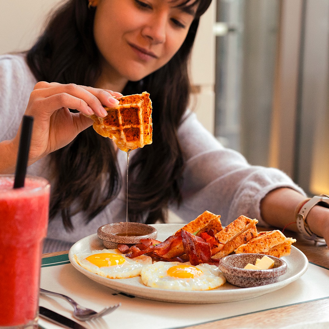 persona sumergiendo un pedazo de waffle en miel